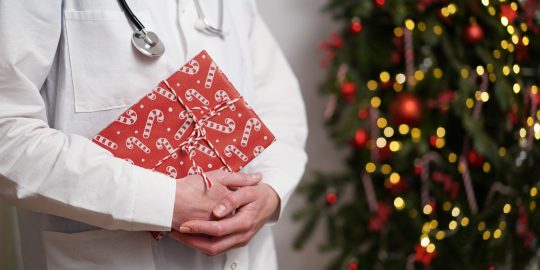 doctor or vet in lab coat carrying present past Christmas tree